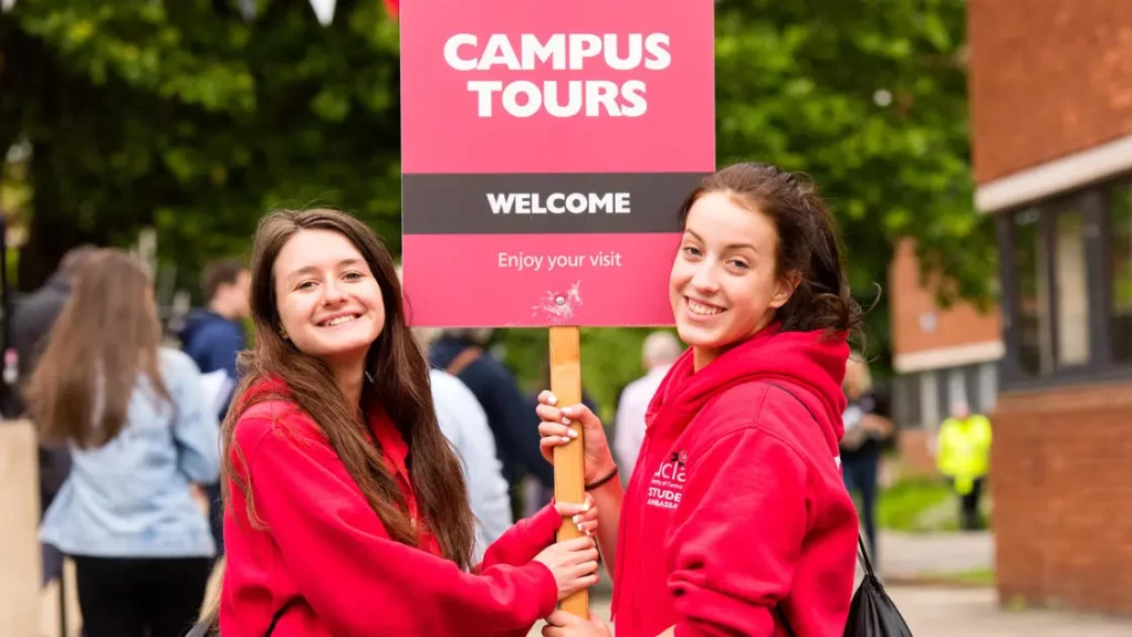 An image of two campus tour guides holding a welcome sign