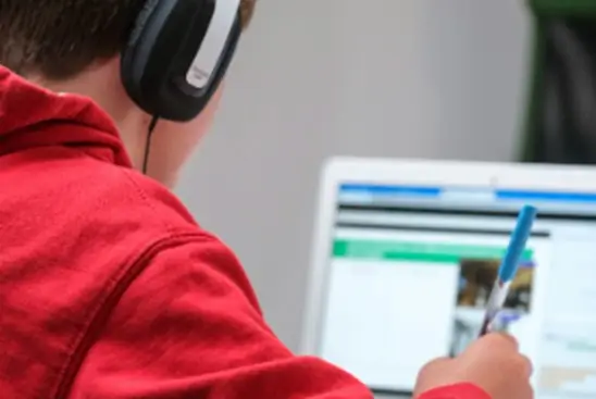 Student in a red hoodie with headphones, using a computer for digital learning