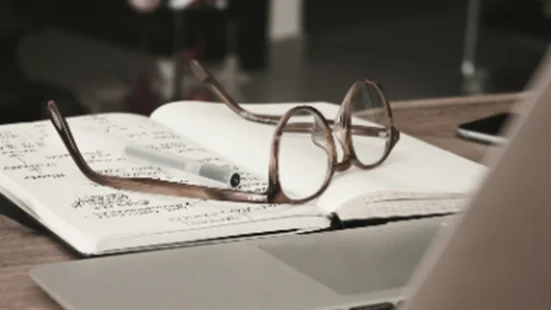 Glasses on an open notebook with handwritten notes and a pen