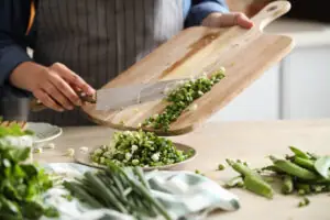 Person is cooking and cutting green onion in pieces